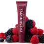 ColourPop Fresh Kiss Glossy Lip Balm tube stands upright amid raspberries, blackberries, and blueberries on a white backdrop, representing the Get Rich ColourPop Glossy Lip Balm Trio with a deep berry-colored tube and high-shine finish.