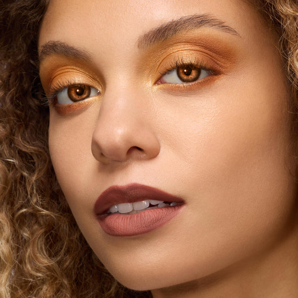 Model showcasing Twilight New Moon x ColourPop Full Collection with shimmering amberβgold eyeshadow, warm copper lower lash line, and matte cocoaβbrown lipstick in a studio closeβup, highlighting pigments from the ColourPop Full Collection Set.
