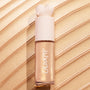 ColourPop Liquid Highlighter Immediately Yes stands upright with a heart-shaped ivory cap and frosted tube, showing a champagne-gold sheen against sweeping metallic swatches, spotlighting the product’s radiant, blendable glow.