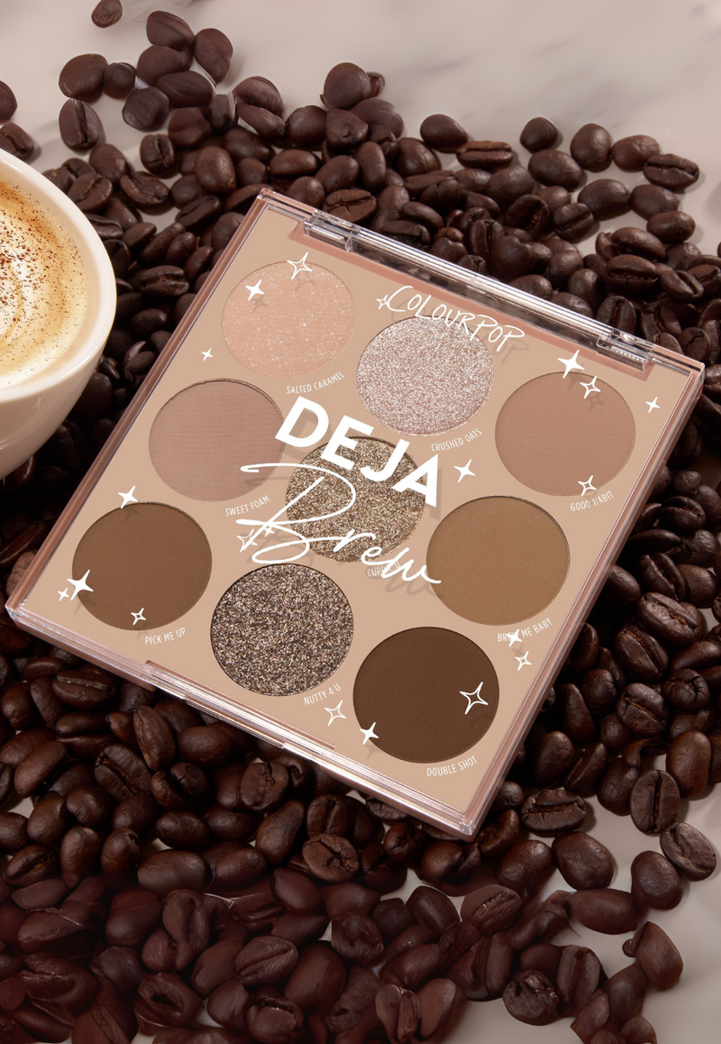 ColourPop Deja Brew eyeshadow palette opens to reveal nine coffee-inspired neutrals - matte and shimmer shades like Salted Caramel and Nutty 4 U - resting on coffee beans beside a foamy latte on a marble counter.