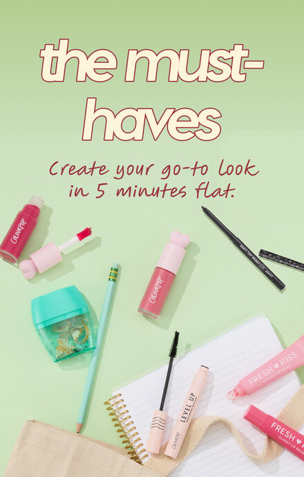 ColourPop makeup must-haves arranged on a pastel green flat lay: Fresh Kiss lip creams, pink doe-foot lip stain, Level Up mascara, two black eyeliners, mint pencil sharpener and pencil, spiral notebook, and canvas pouch, promoting a 5-minute go-to look.