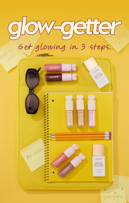 ColourPop Glow-Getter back-to-school flatlay featuring SOL body highlighter, multiple pastel lip gloss tubes, sunglasses, notebook, and pencils arranged on a yellow laptop sleeve against a bright yellow background with sticky notes.