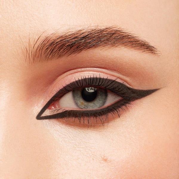 Defined black lashes coated with ColourPop BFF Mascara in Black on Black, fanning a blue‑gray eye framed by bold graphic double‑wing eyeliner; close‑up beauty shot showcasing clump‑free length and volume.