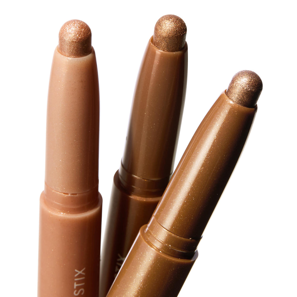 Shimmering Golds ColourPop Shadow Stix trio showing uncapped metallic gold and bronze cream eyeshadow tips catching light, angled side by side in a macro close-up on white, highlighting twist-up crayon packaging for quick swipe-on eye looks.