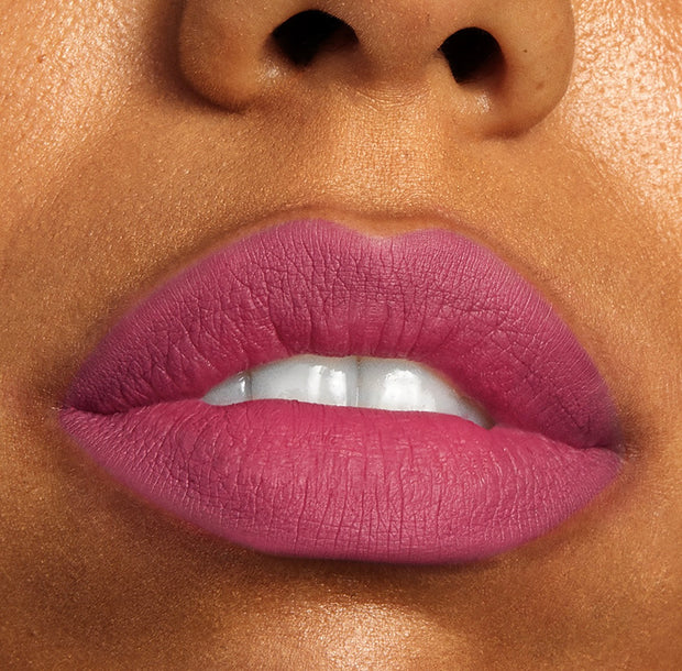 Rosy-mauve lips wearing ColourPop Lippie Stix Byron Babe, showcasing smooth, full-coverage soft-matte color on slightly parted lips with teeth visible in a tight close-up.