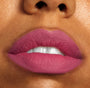 Rosy-mauve lips wearing ColourPop Lippie Stix Byron Babe, showcasing smooth, full-coverage soft-matte color on slightly parted lips with teeth visible in a tight close-up.