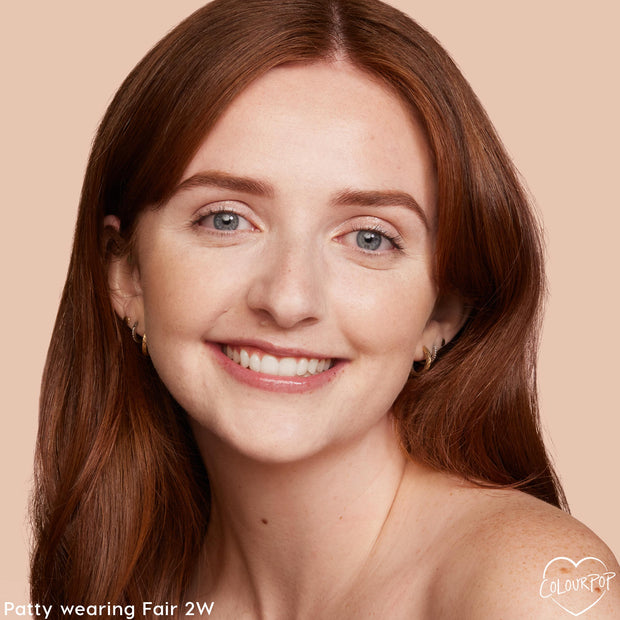 Model wearing ColourPop Pretty Fresh Tinted Moisturizer in Fair 2 W, smiling in a close-up against a beige backdrop, showing a smooth, natural, light-coverage finish with a subtle glow; auburn hair, minimal makeup, ColourPop logo in corner.