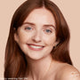 Model wearing ColourPop Pretty Fresh Tinted Moisturizer in Fair 2 W, smiling in a close-up against a beige backdrop, showing a smooth, natural, light-coverage finish with a subtle glow; auburn hair, minimal makeup, ColourPop logo in corner.
