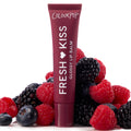 ColourPop Fresh Kiss Glossy Lip Balm tube stands upright amid raspberries, blackberries, and blueberries on a white backdrop, representing the Get Rich ColourPop Glossy Lip Balm Trio with a deep berry-colored tube and high-shine finish.