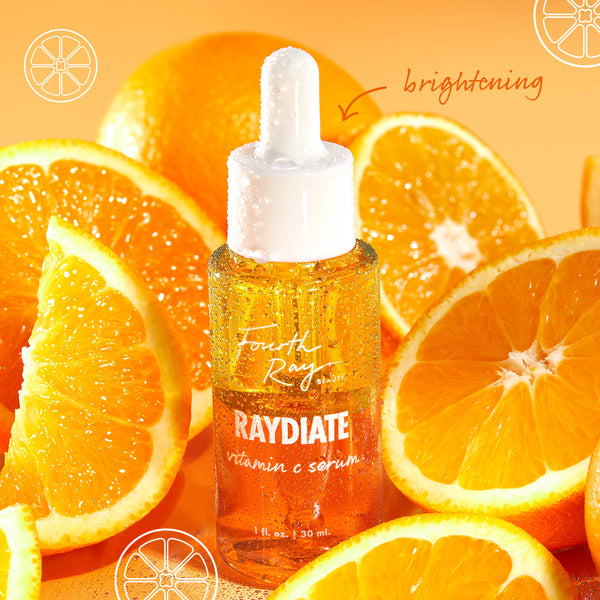 RAYdiate Vitamin C Serum by Fourth Ray Beauty (ColourPop Face Serum) displayed as a dewy dropper bottle beaded with condensation, standing among juicy orange slices on a bright orange backdrop, emphasizing a brightening, glow-boosting formula.