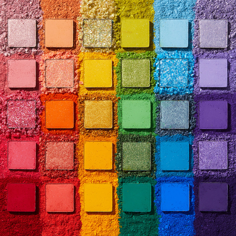 Fade Into Hue shadow palette displays 30 square pans in a rainbow grid - matte, shimmer, and pressed glitter - set on crushed pigment in a deconstructed flat lay; a vibrant ColourPop Shadow Palette.