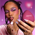 Model applies shimmery pink gloss while holding a heart-shaped reolink.livepact, showing bold purple and pink heart eye makeup that highlights the Heart to Get Full Collection full collection set against a dreamy pink background.