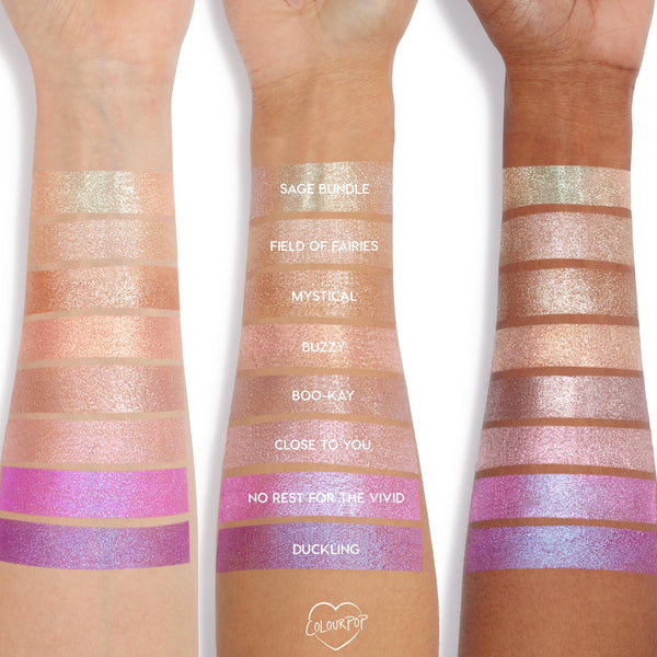 Buzzy Jelly Much Shadow swatched on three arms, showing a peachy rose-gold shimmer stripe among labeled shades; the ColourPop Jelly Much Shadow jelly-gel eyeshadow reflects metallic sparkle across light to deep skin tones.