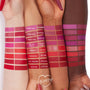 Byron Babe ColourPop Lippie Stix swatched on three arms, showcasing its rosy mauve shade among labeled swatches, with a Lippie Stix pen held near the wrists and a ColourPop heart logo on a white background.