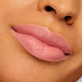 Lips wearing ColourPop Lippie Stix NBD in a soft pink-nude shade, displaying creamy satin coverage and subtle sheen; tight close-up swatch on medium-tan skin to show color payoff and smooth application.