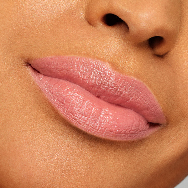 Lips wearing ColourPop Lippie Stix NBD in a soft pink-nude shade, displaying creamy satin coverage and subtle sheen; tight close-up swatch on medium-tan skin to show color payoff and smooth application.