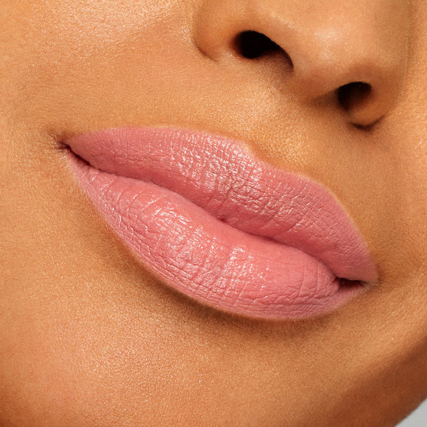 Lips wearing ColourPop Lippie Stix NBD in a soft pink-nude shade, displaying creamy satin coverage and subtle sheen; tight close-up swatch on medium-tan skin to show color payoff and smooth application.