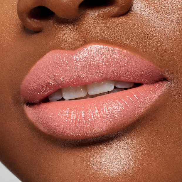 Lips wearing ColourPop Lippie Stix in NBD, a soft pink-peach nude, delivering creamy satin coverage with a subtle sheen; close-up beauty shot emphasizing smooth texture and moisturized finish.