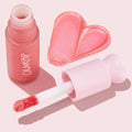 ColourPop Liquid Blush I Love It swatches a shimmery pink heart, with the doe-foot applicator and heart-topped pastel cap next to a frosted rosy bottle on a soft pink background.