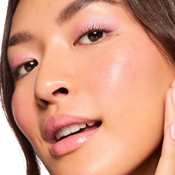 Dewy cheekbone glowing as Pink Pony liquid highlighter catches light, showcasing ColourPop Liquid Highlighter on the high points; soft pink eyeshadow and glossy lips complete the look in a close-up beauty macro against a white background.