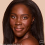 Smiling model showcases ColourPop Pretty Fresh Tinted Foundation Balm, shade Deep Dark 24, with smooth, even, natural coverage and a subtle glow in a close-up against a warm beige studio background.