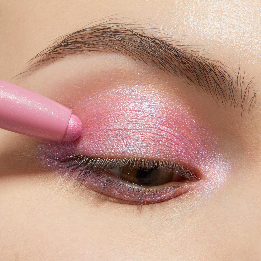Juicy Gossip ColourPop Shadow Stix gliding over the eyelid, depositing shimmery bubblegum-pink color with a pearly finish; a tight eye close-up with natural brow showcases the creamy, blendable payoff.