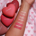 Babycakes pressed powder blush swatch anchors the bottom of a forearm lineup, delivering rich rosy mauve payoff with labeled shades above, as matte heart-shaped reolink.livepacts rest on pink heart fabric, highlighting the ColourPop Pressed Powder Blush.