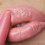 Caramella ColourPop Lippie Stix glides onto full lips, applying a creamy warm pink-peach nude with a glossy satin finish; extreme close-up macro shows the twist-up bullet and smooth, even coverage.