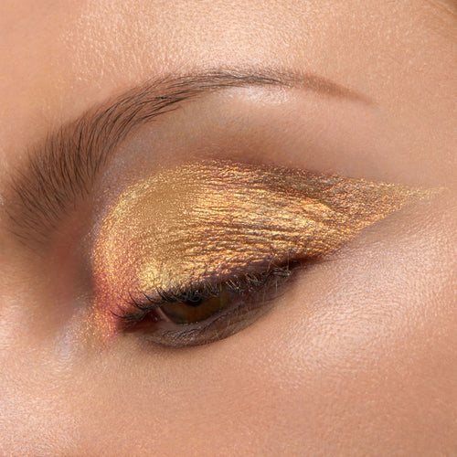 ColourPop Chrome Liquid Shadow in Sweetzer Ave swept across a closed eyelid, flashing molten gold with rose-copper shifts in a sharp wing, showcasing high-shine metallic finish and smooth, opaque payoff in a studio close-up.