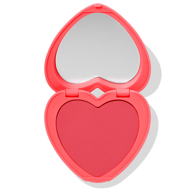 Heart-shaped Woo Me compact opens to reveal a matte rosy-pink pan and built-in mirror, set in a bright coral case on a white background - ColourPop Pressed Powder Blush for a flirty, Valentine-ready flush.
